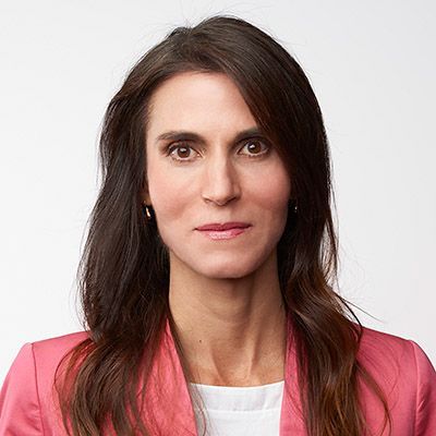 Woman with long brown hair wearing a pink jacket.
