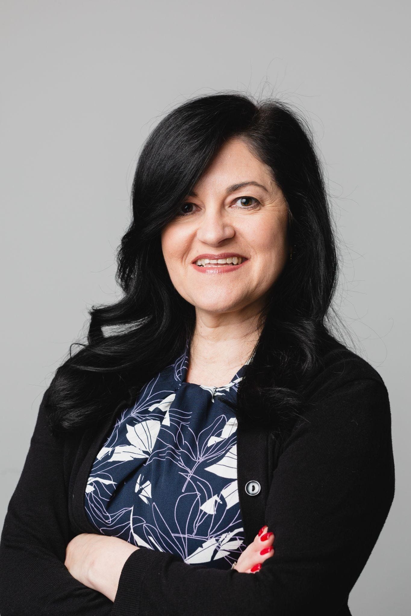 Woman with black hair and a black sweater smiles, arms crossed.