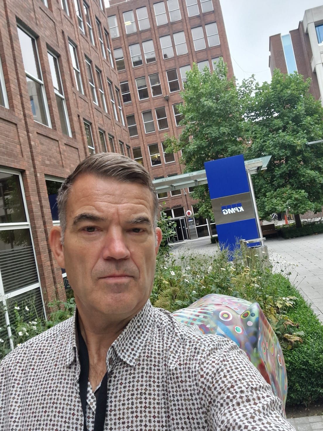 A man is taking a selfie in front of a large building.
