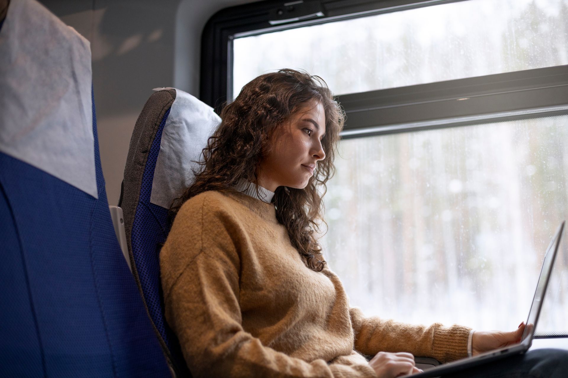 Mulher trabalhando em um laptop enquanto anda de trem, olhando pela janela.