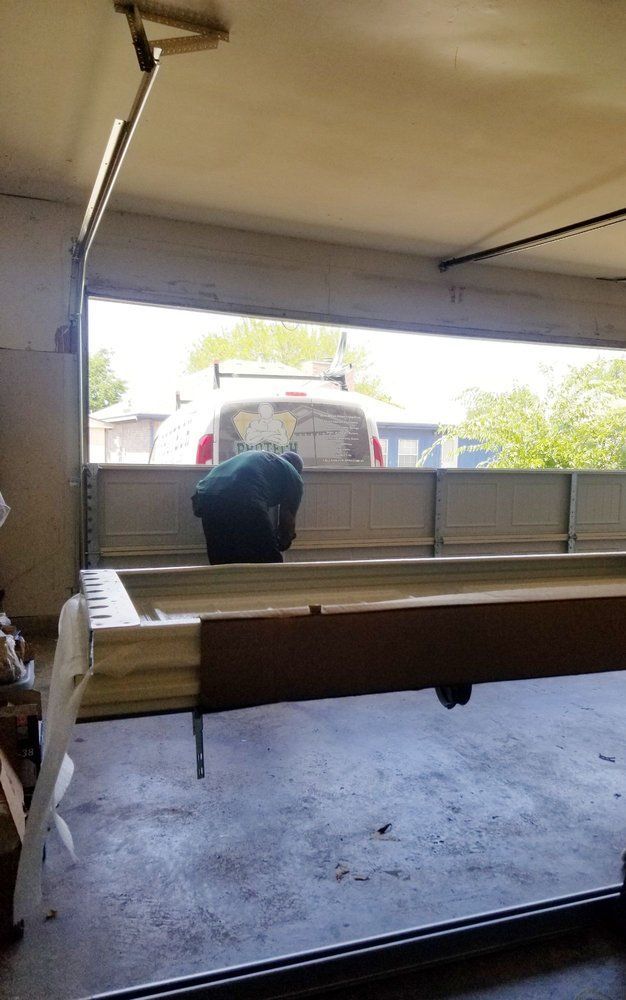 Person loading a large wooden board into a garage beside a white van.
