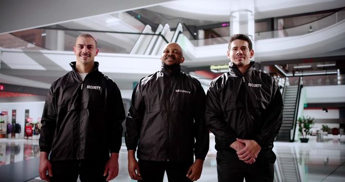 Three men in black jackets standing in a modern indoor atrium with curved architecture.