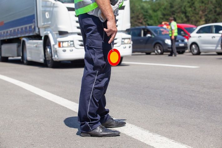 Traffic officer standing on a road directing vehicles near a truck and parked cars