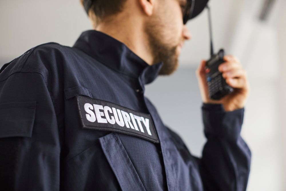 Security guard in a dark uniform speaking into a handheld radio indoors