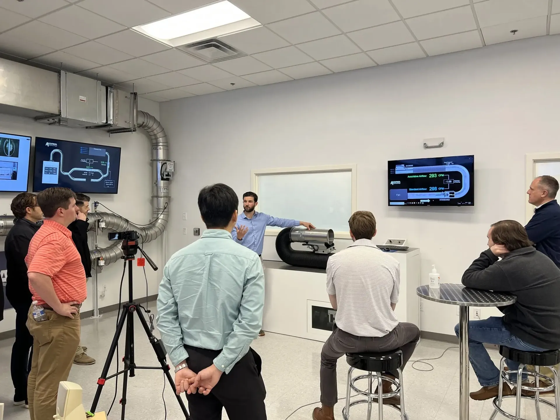 People gathered in a room for a presentation, watching screens and a speaker at the front.