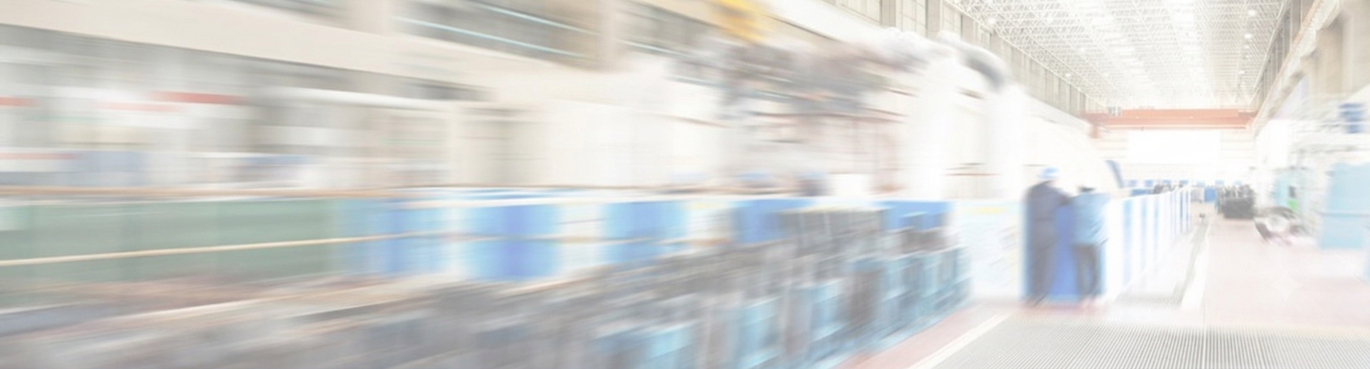 Bright indoor factory or warehouse aisle with machinery, blue equipment, and a person walking in the distance