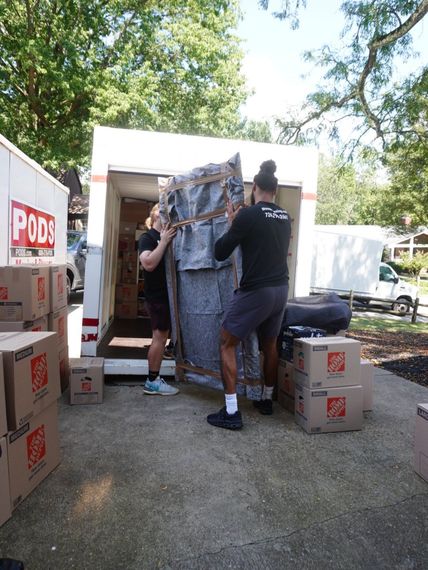 Two people loading items for a small move into a PODS storage container outdoors
