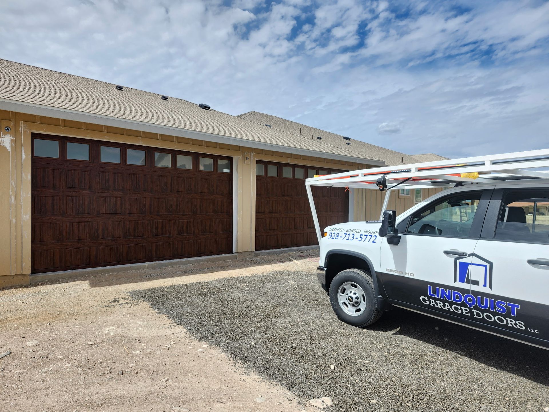 Brown garage doors on a tan house with a company truck in front, under a cloudy sky.