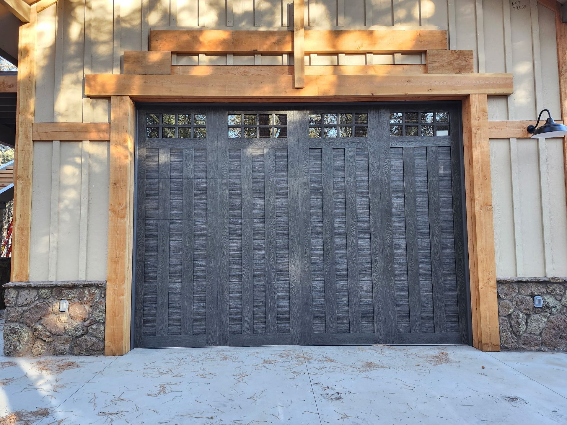 Gray textured garage door framed by wood, with stone base and wood trim.