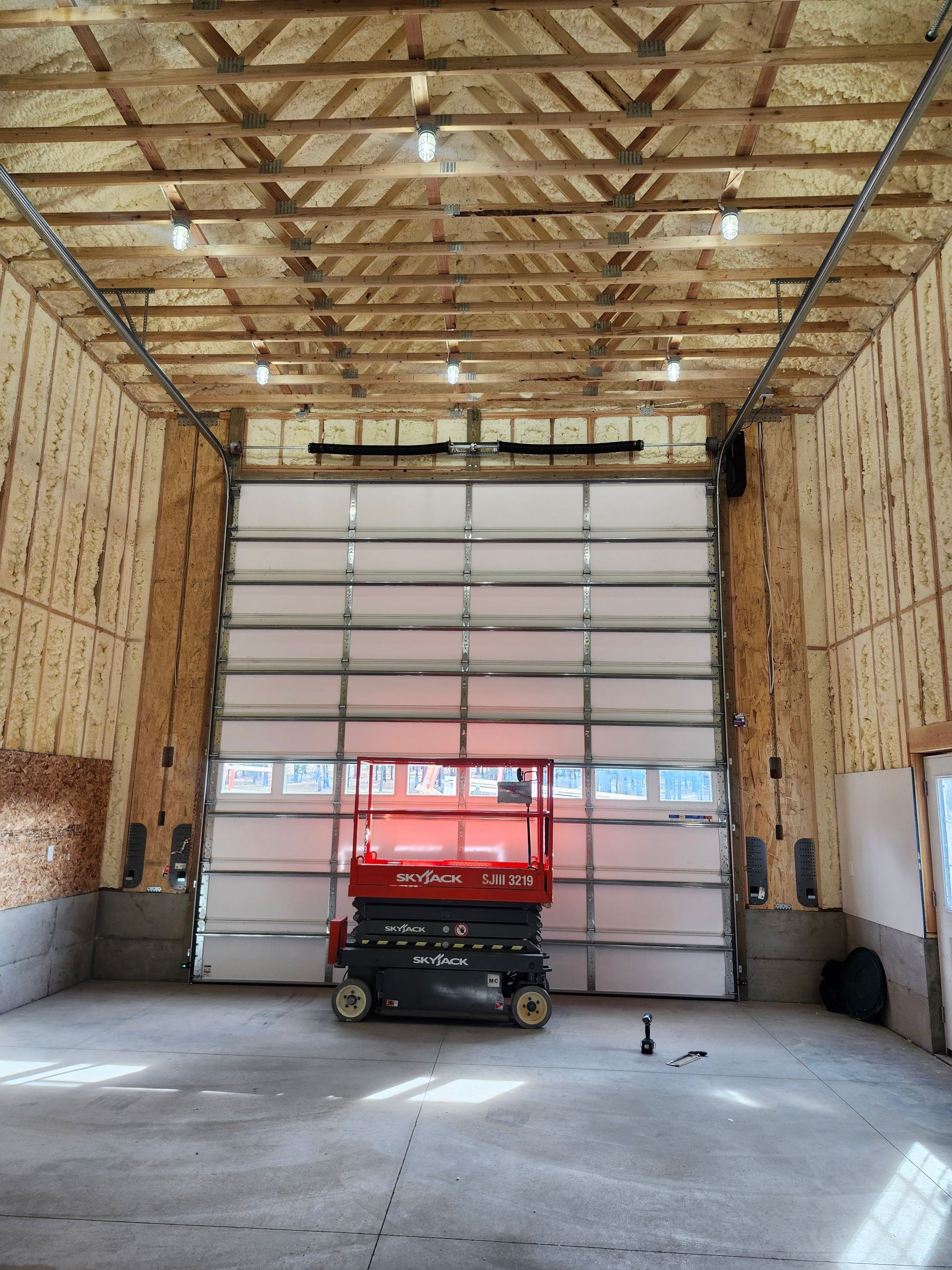 Red scissor lift inside a large garage with a closed overhead door and exposed wooden beams.