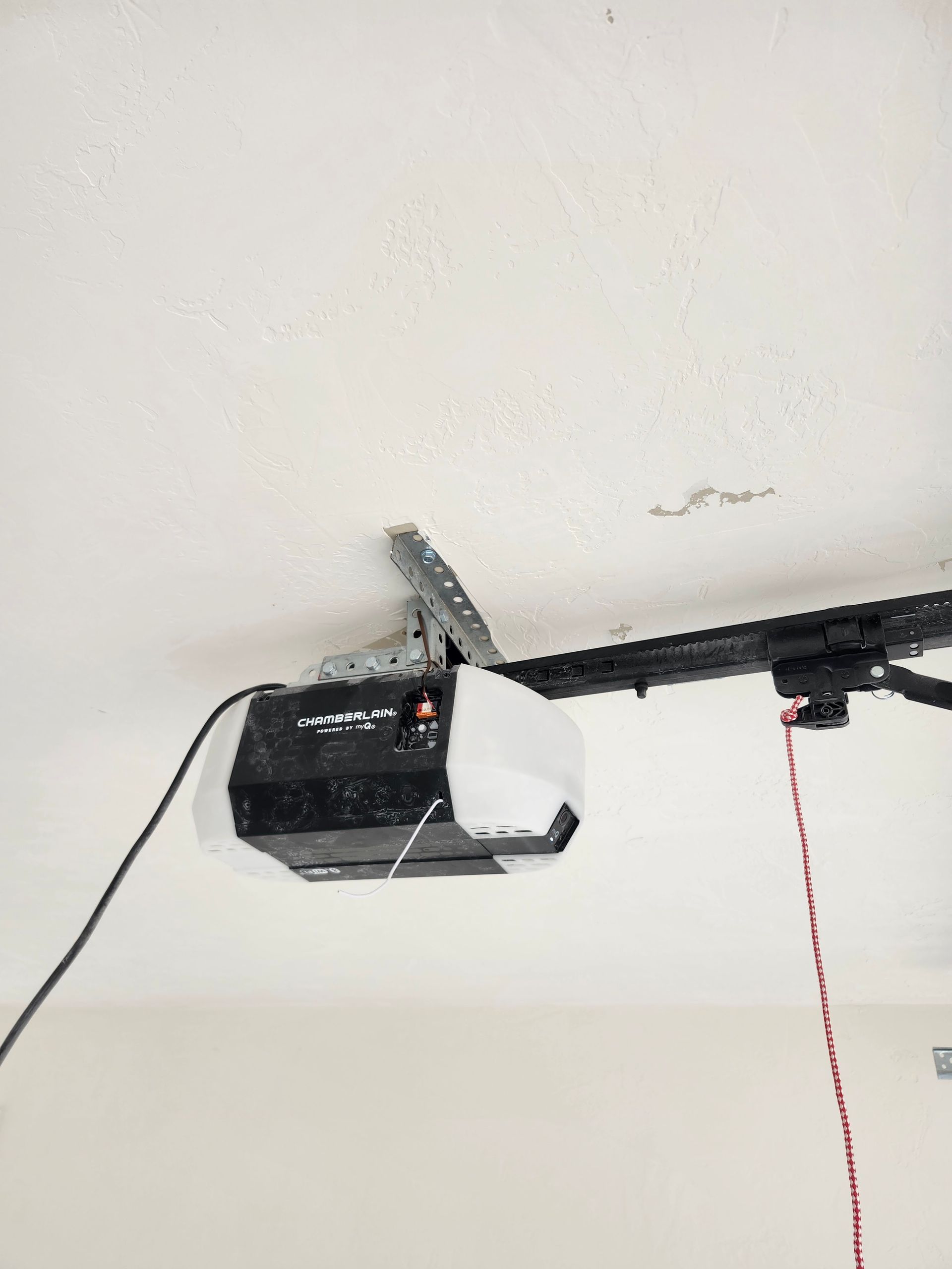 Garage door opener attached to the ceiling, black and white, with a red emergency release cord.