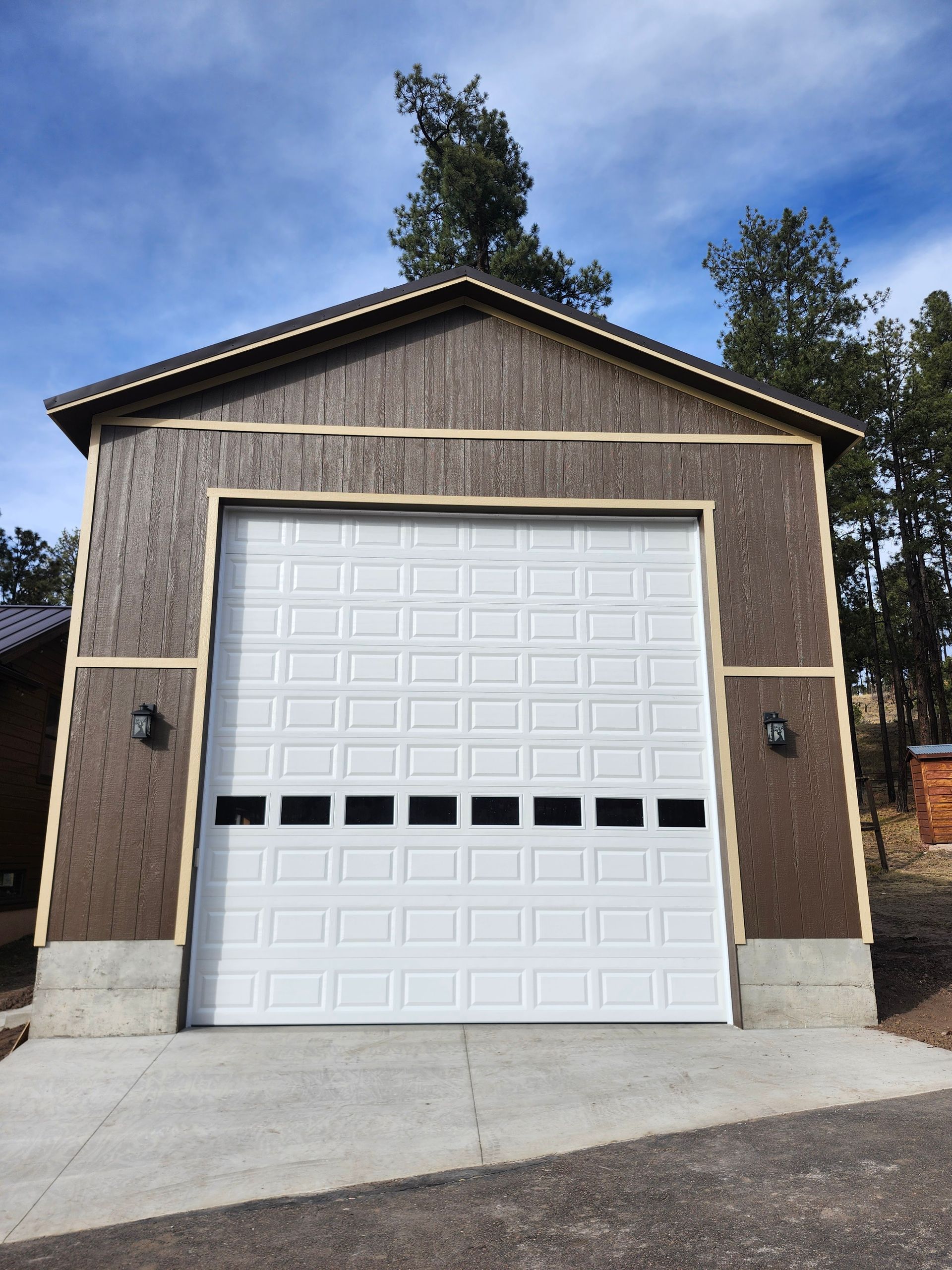 White garage door on a brown building with concrete base, under a blue sky.