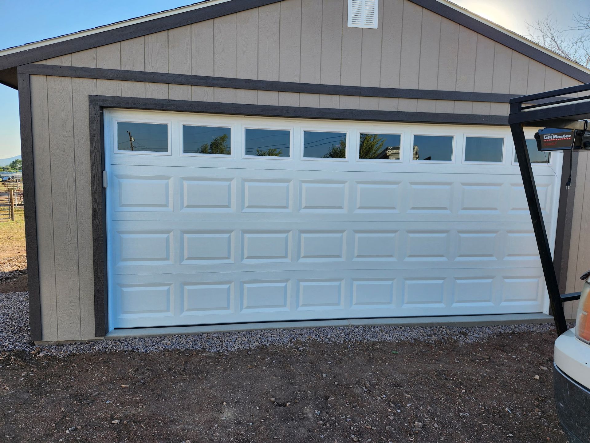 White garage door with windows, on a tan building with brown trim.