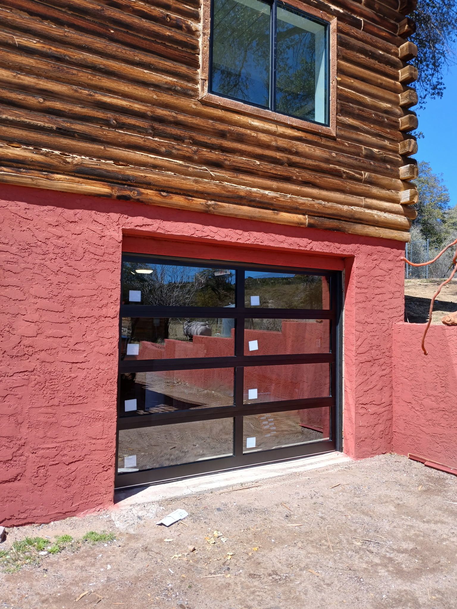 Log cabin exterior with red stucco, a black-framed glass garage door, and a window above.