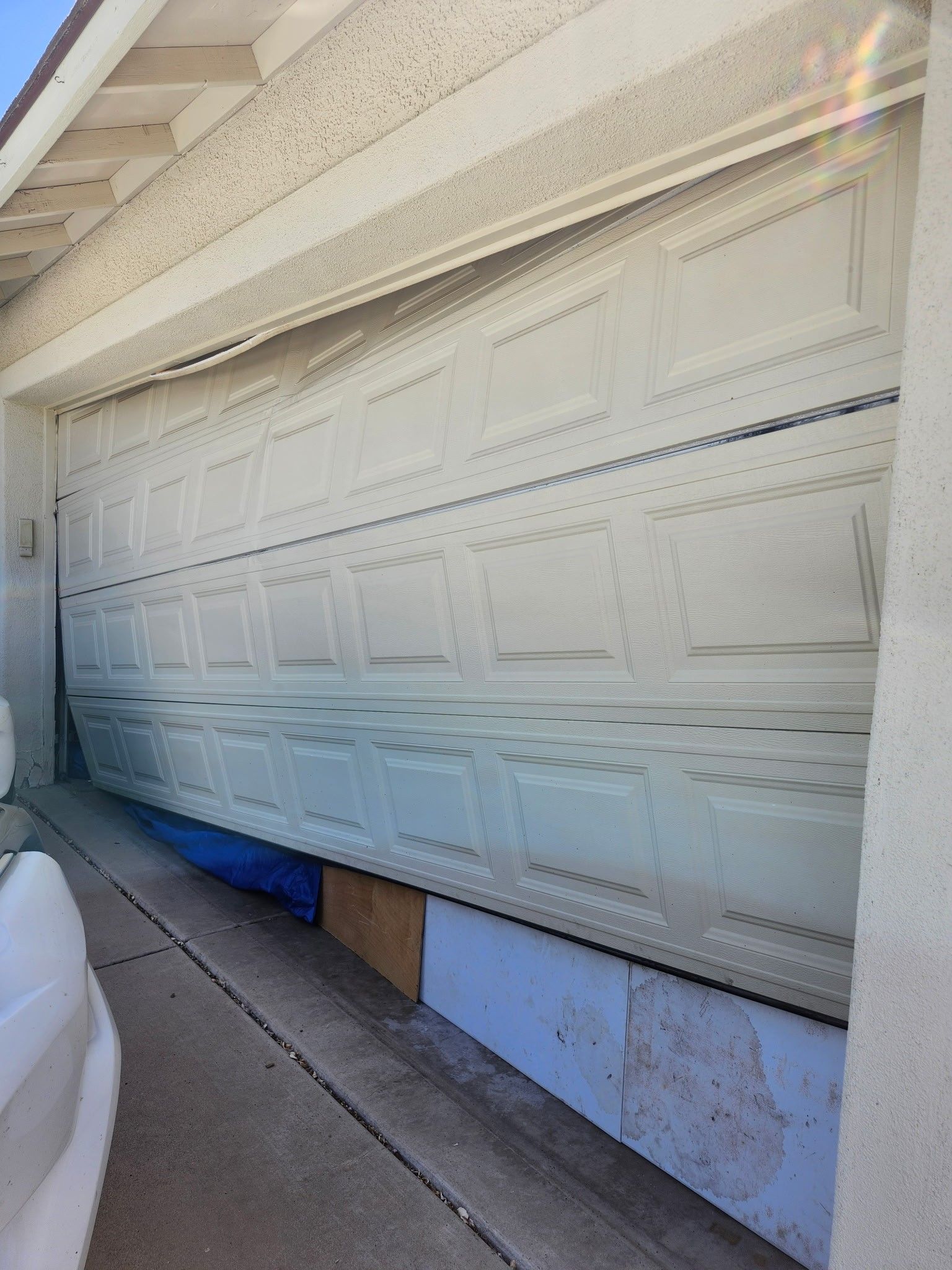 Damaged white garage door, partially open and bent inward.