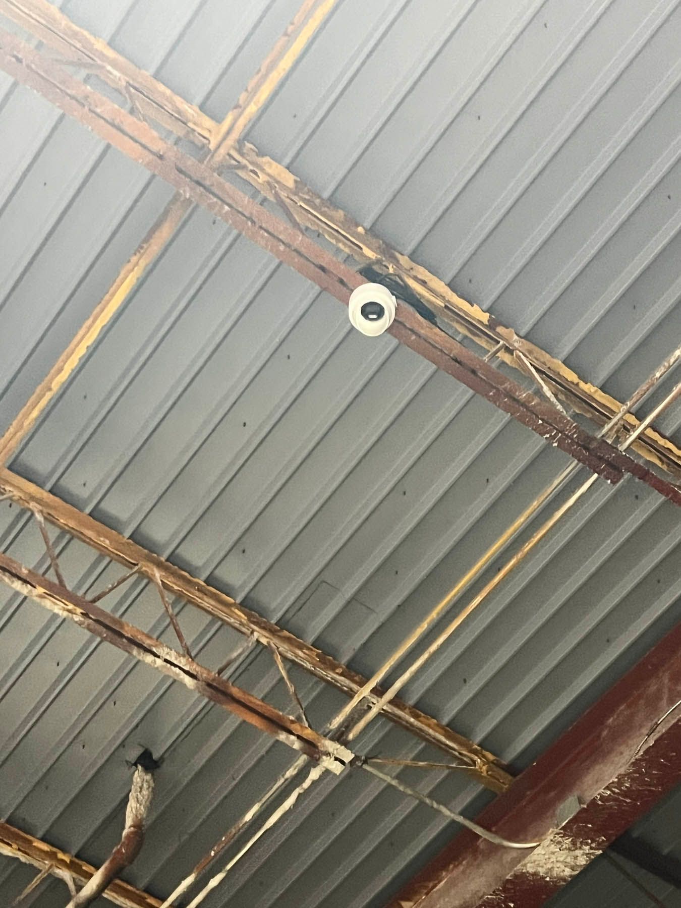 A security camera mounted on a deteriorating metal roof with exposed wooden beams.