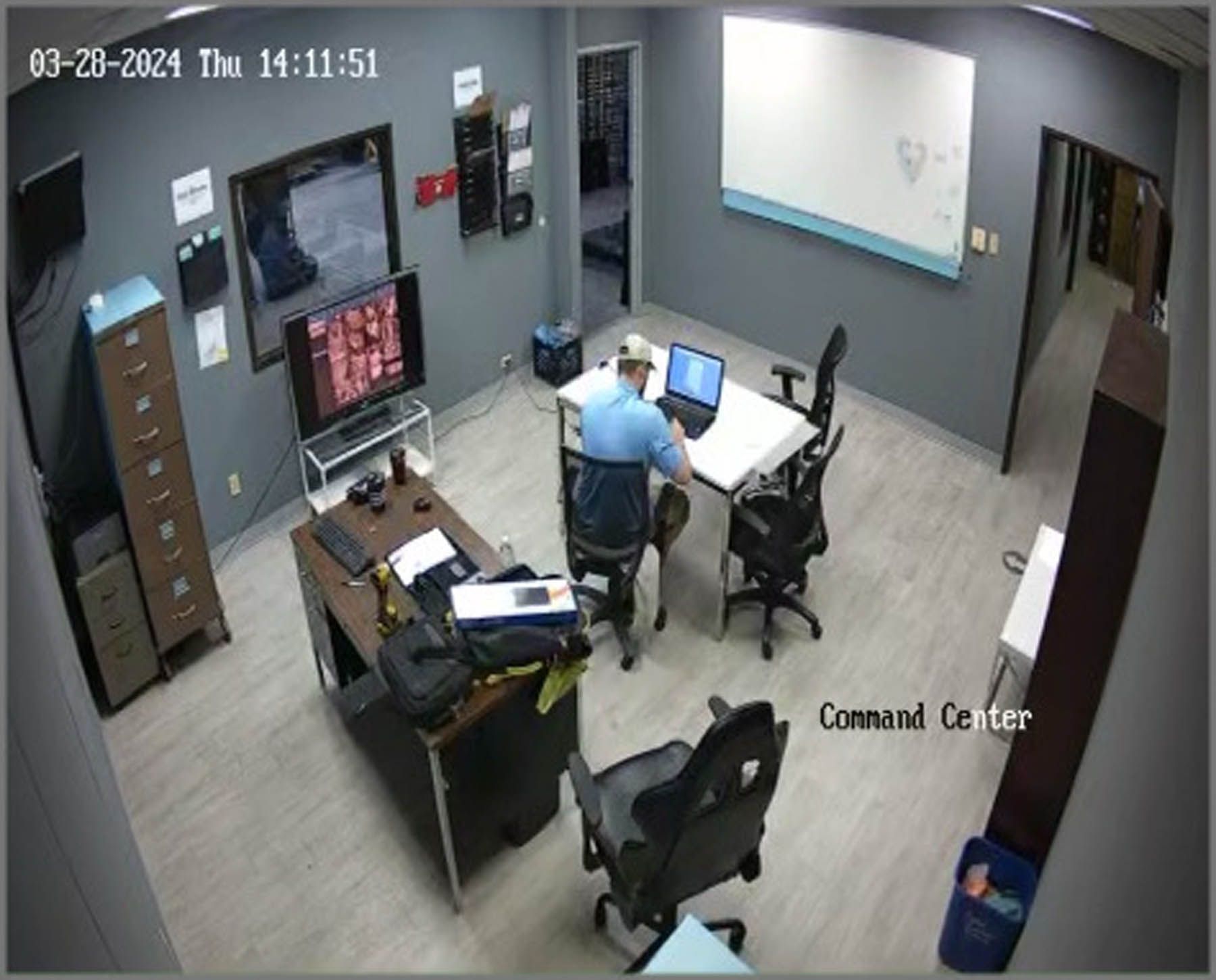 A person in a command center, working at a computer, with monitors and whiteboard visible.