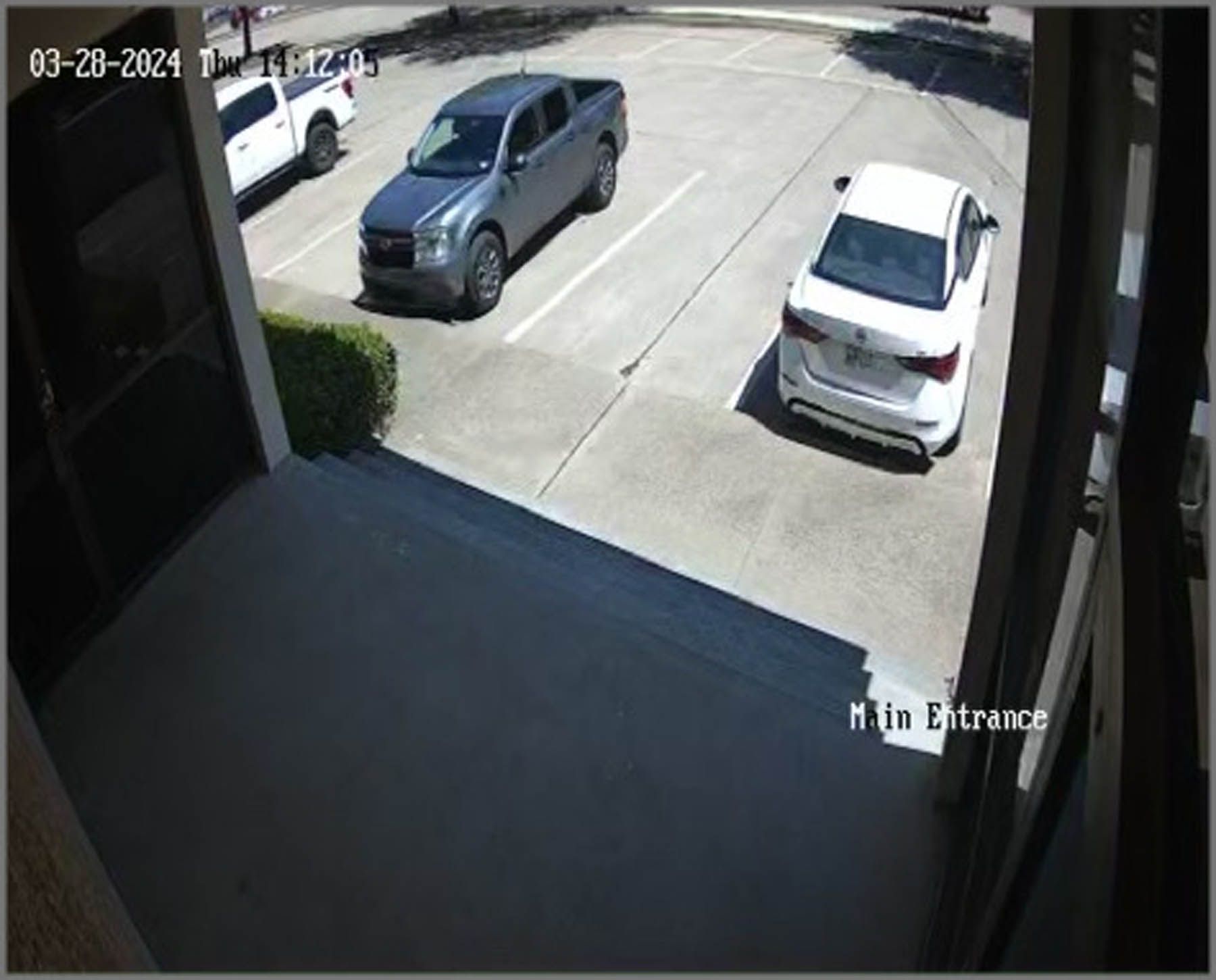 Parking lot scene: Gray truck and white car parked. A white truck is in the background. 