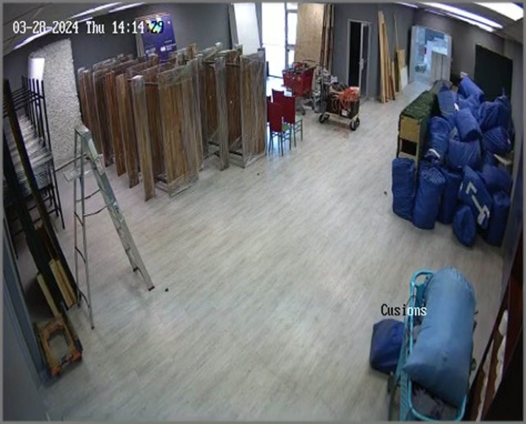 Warehouse interior with wooden panels, stacks of blue bags, and a person near a window.