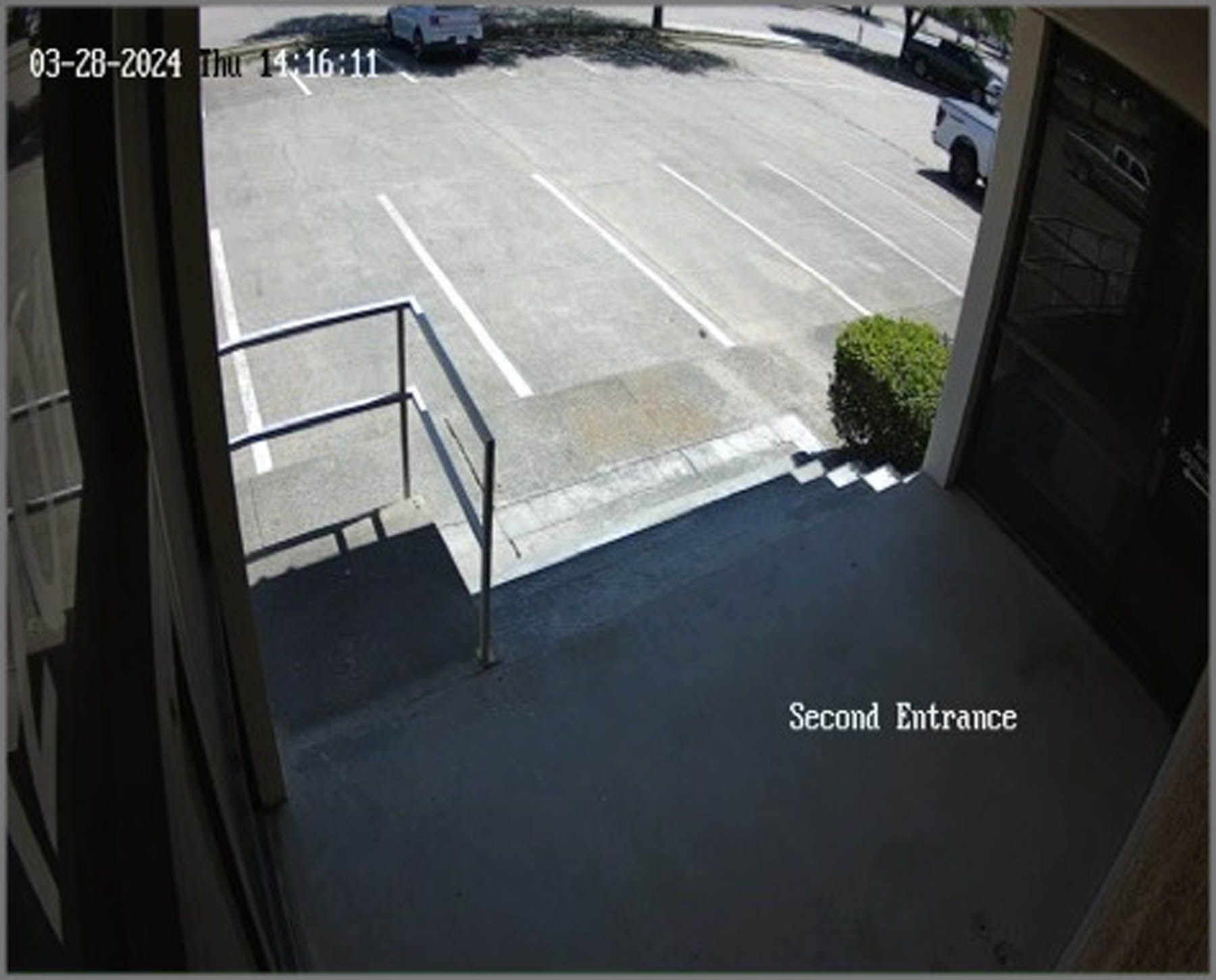 View from a second entrance doorway with steps leading to a parking lot; a car and truck parked outside.