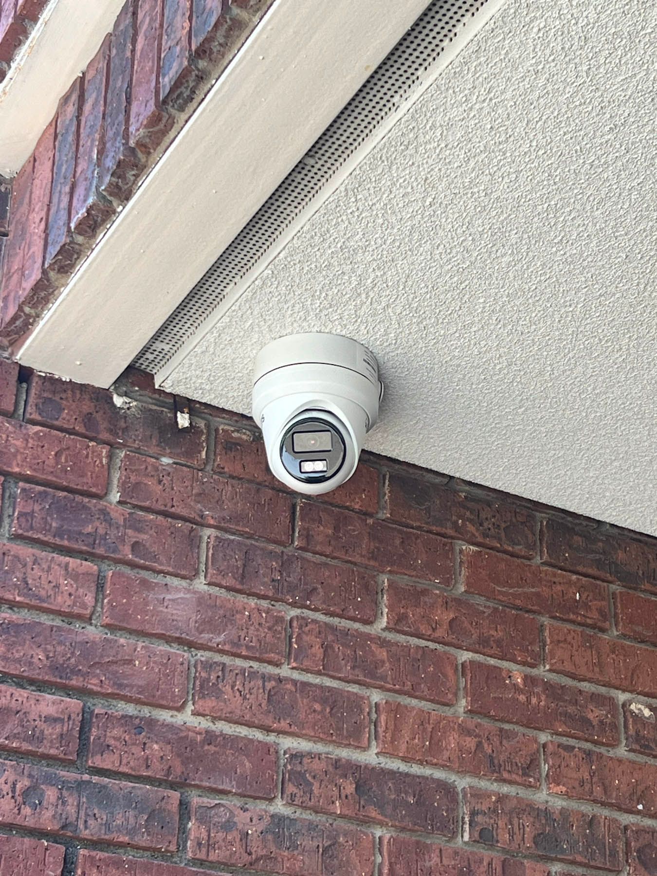 Security camera mounted on a red brick wall under a textured white ceiling.