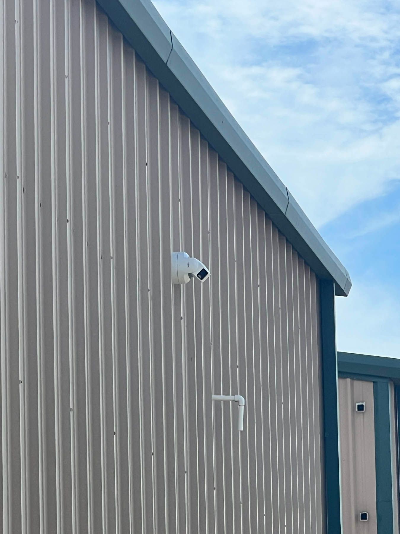 Security camera mounted on a corrugated metal building wall, under a blue sky.