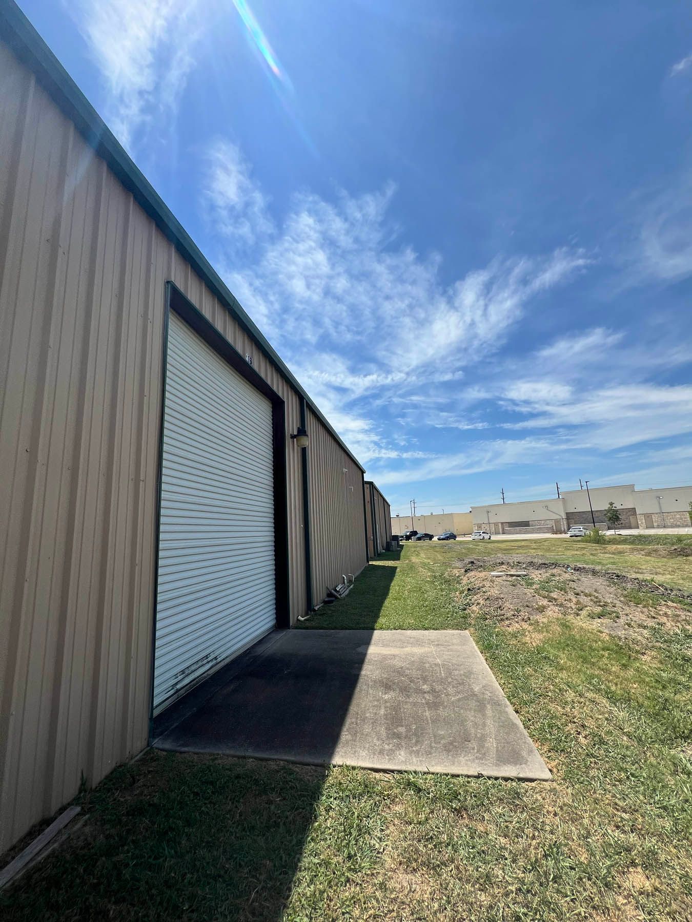 Exterior view of storage units with rolling doors, under a partly cloudy sky.