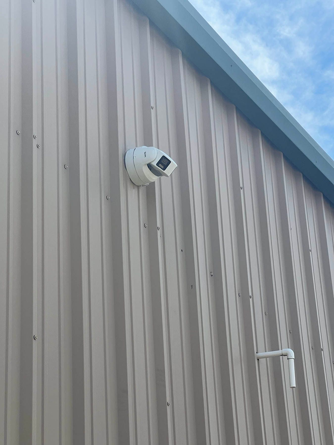 White security camera mounted on a tan corrugated metal building exterior.