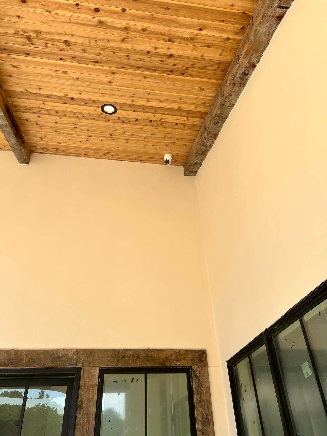 Interior corner with wood ceiling, security camera, and windows with black frames.