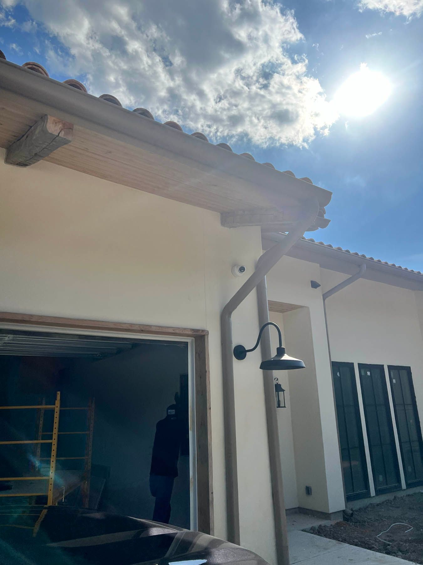 Exterior of a light-colored stucco building with a clay tile roof and a black outdoor light fixture.