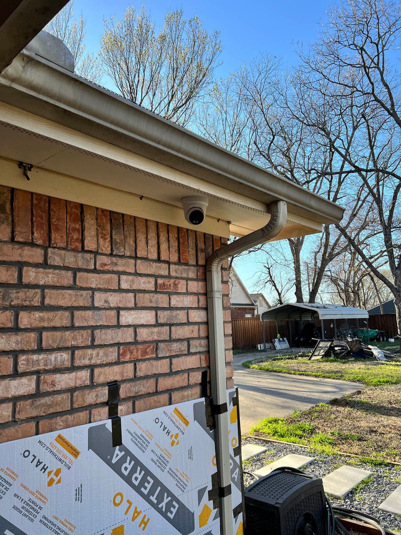 Security camera mounted under a beige gutter on a brick wall, with a downspout.