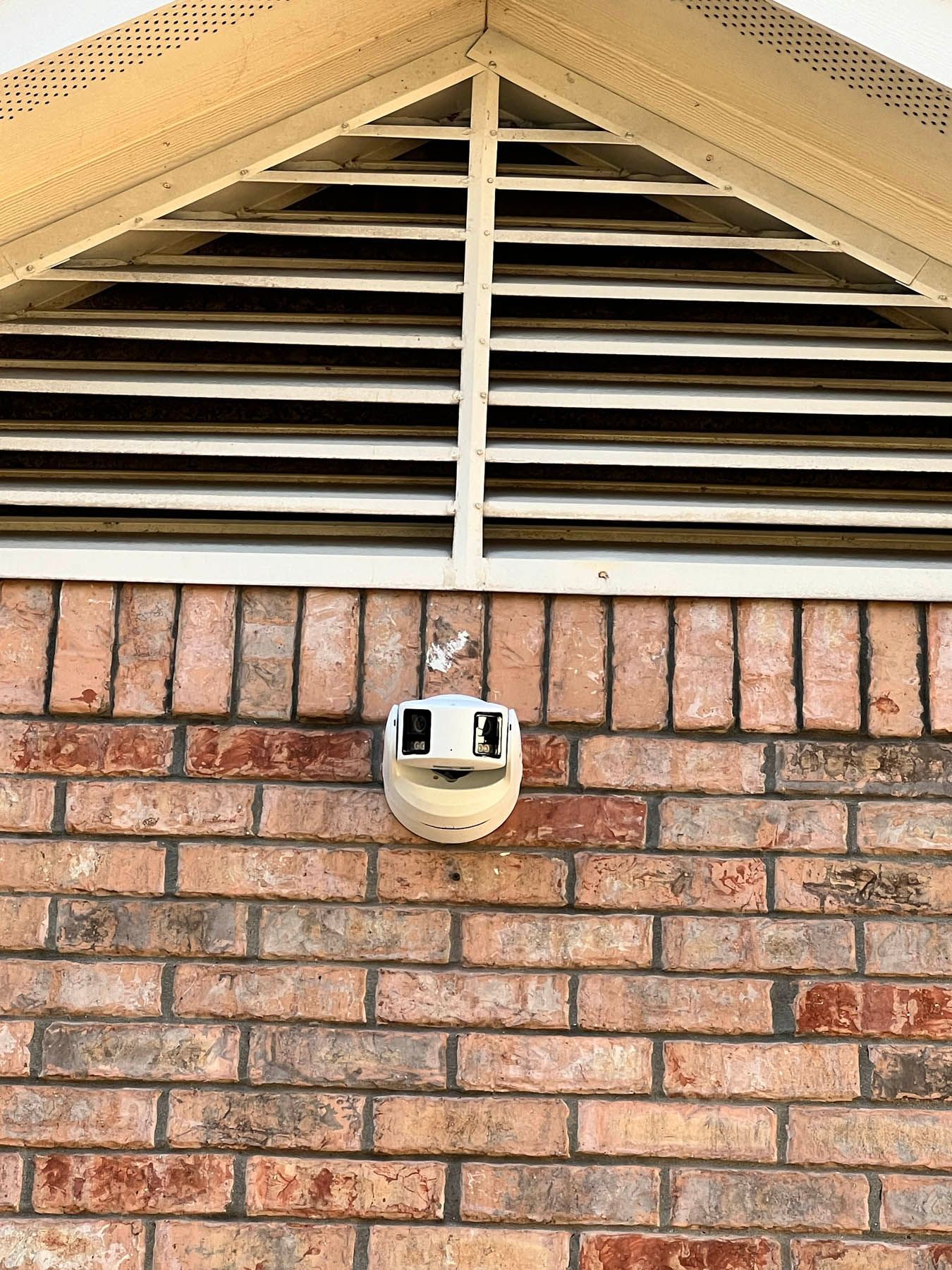 Brick building exterior with a security camera mounted below a ventilation vent.
