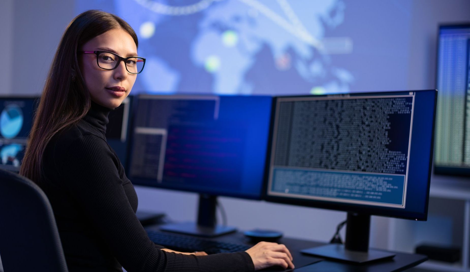 A woman is sitting at a desk in front of a computer monitor.