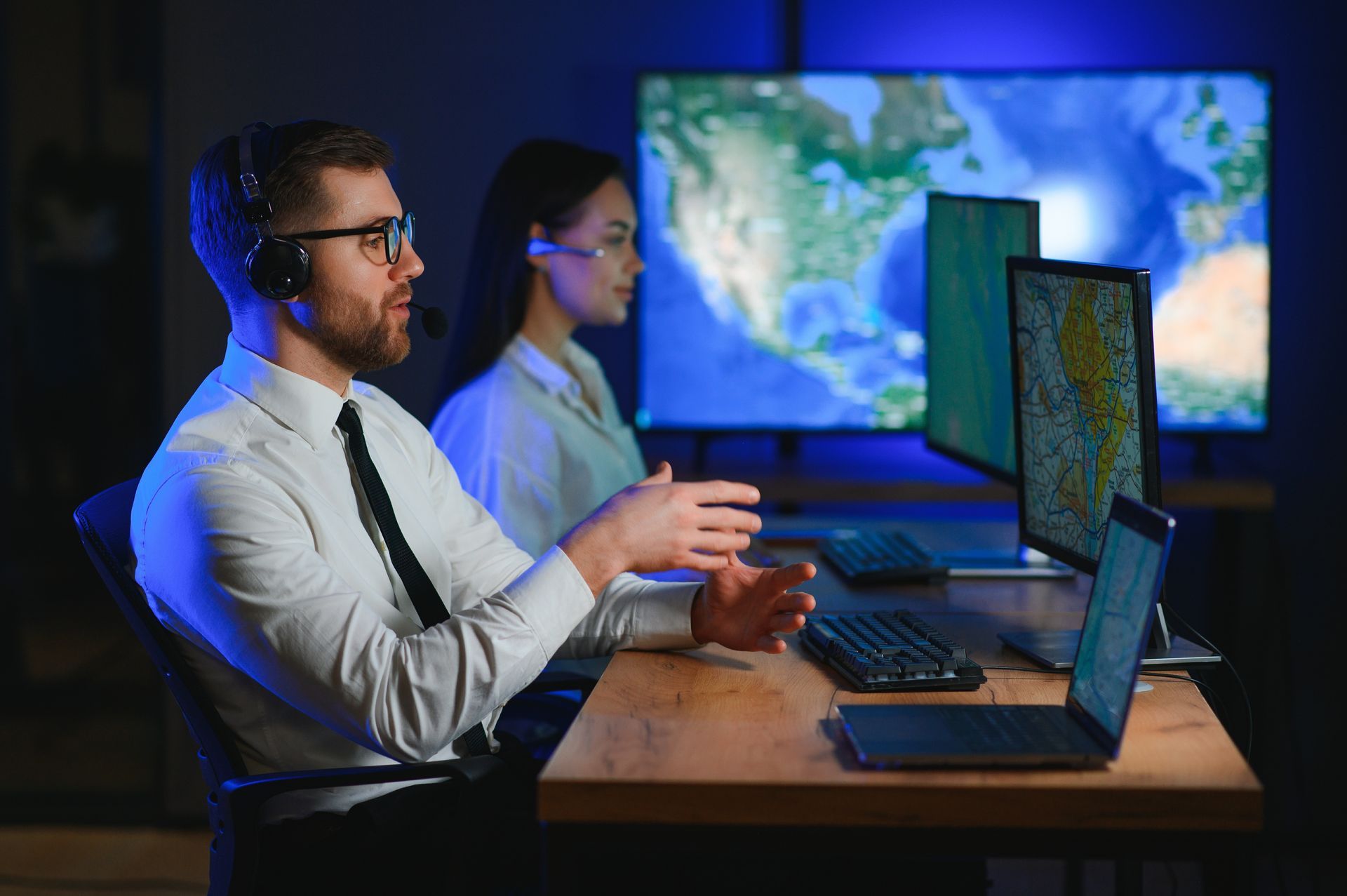 A man and a woman are sitting at a desk in front of computer monitors.