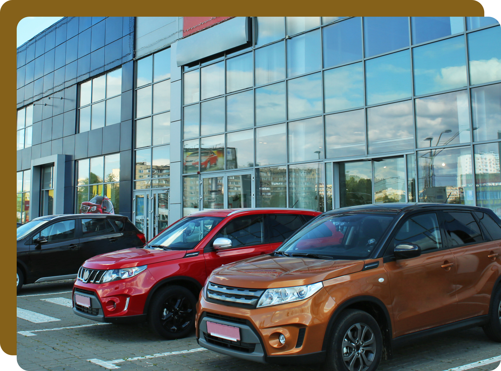 Cars parked in front of a modern building with large windows; red, brown, and black vehicles.