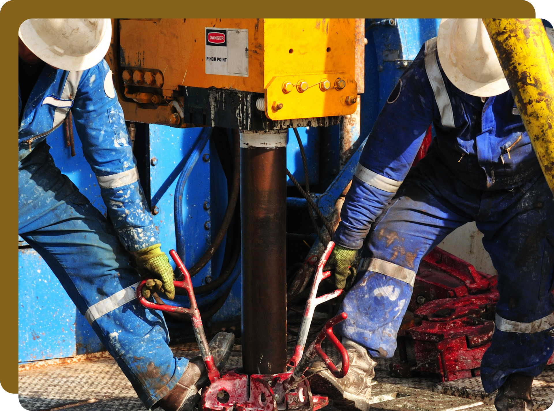 Two workers in blue coveralls operate oil drilling equipment.