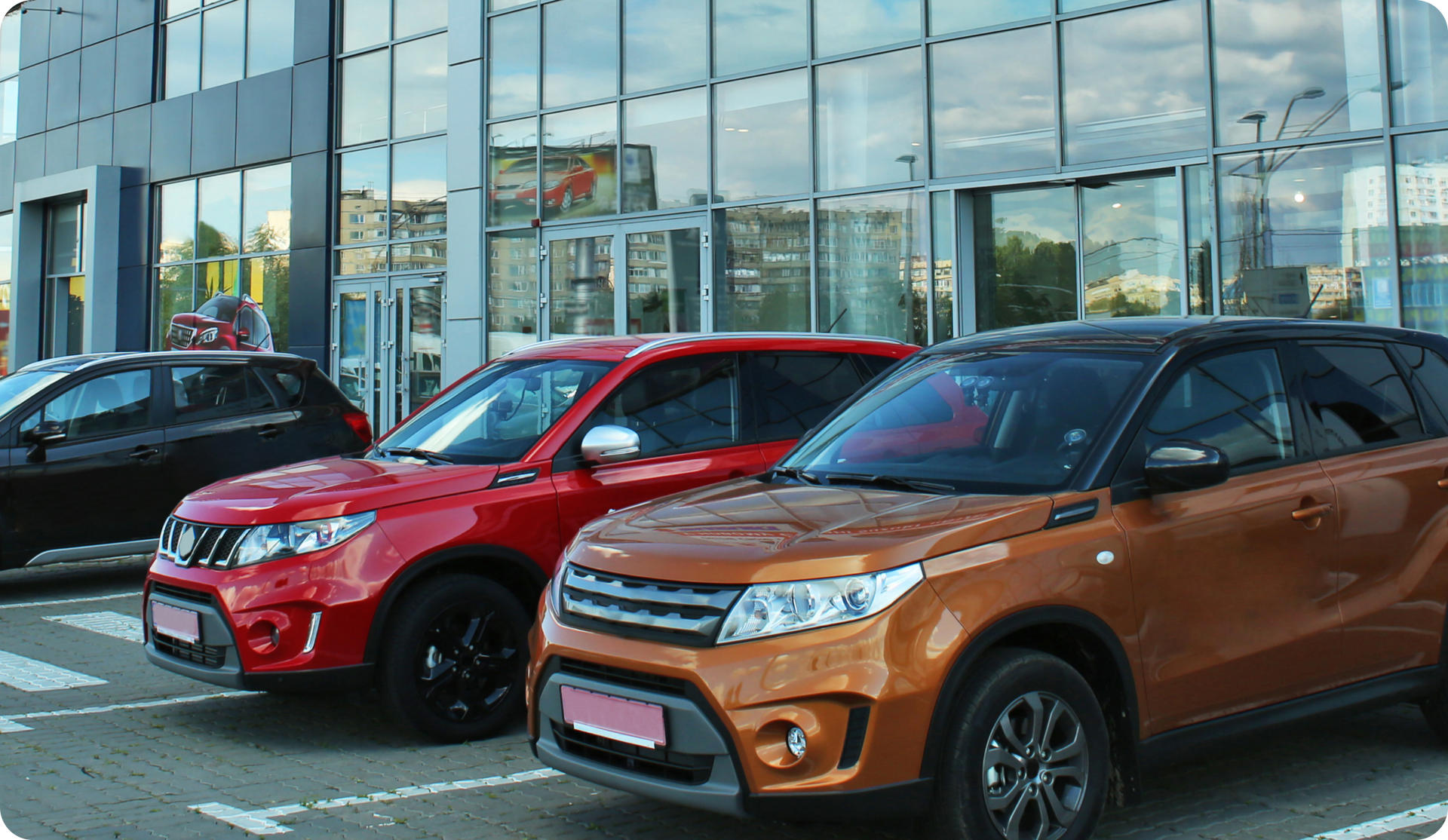SUVs parked outside a car dealership. A red, orange, and black SUV are in front.
