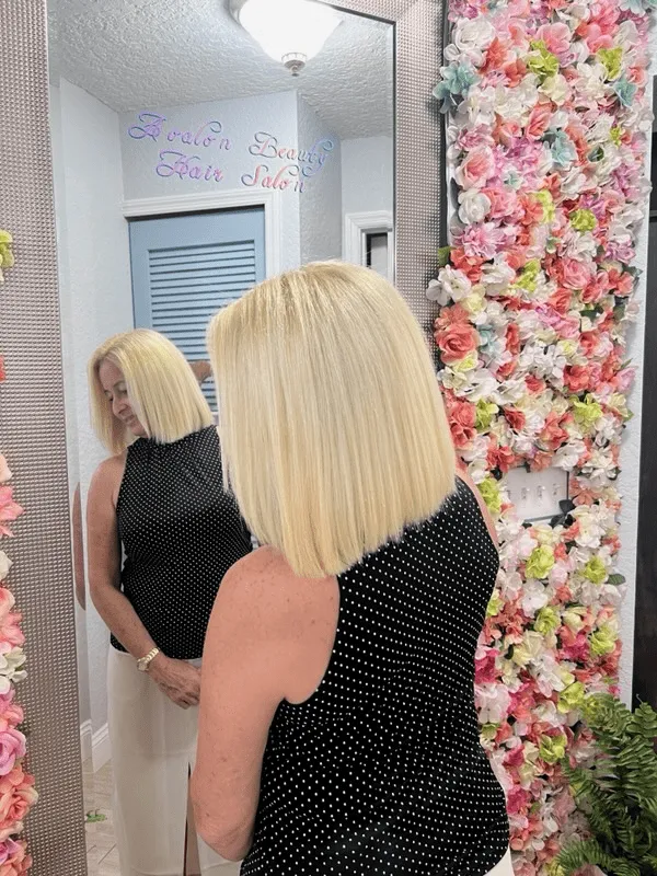 A woman is looking at herself in a mirror in front of a wall of flowers.