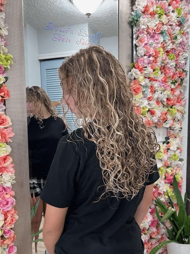 A woman is standing in front of a mirror with flowers on the wall behind her.