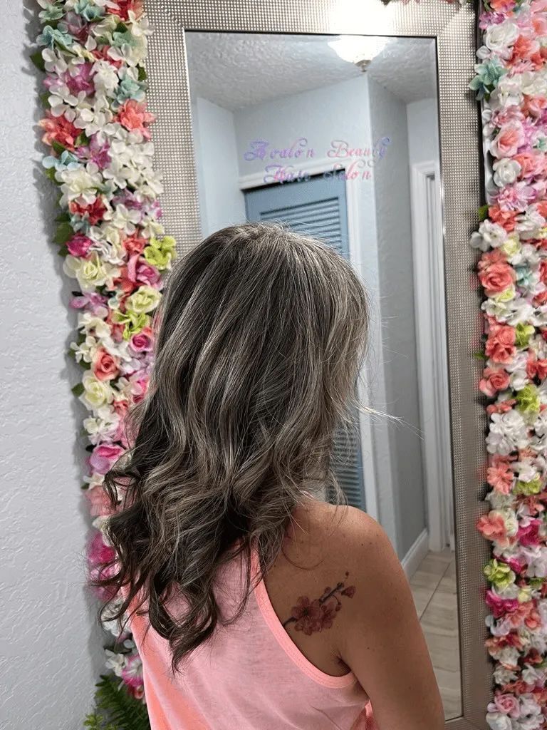 A woman is standing in front of a mirror with flowers on the wall behind her.