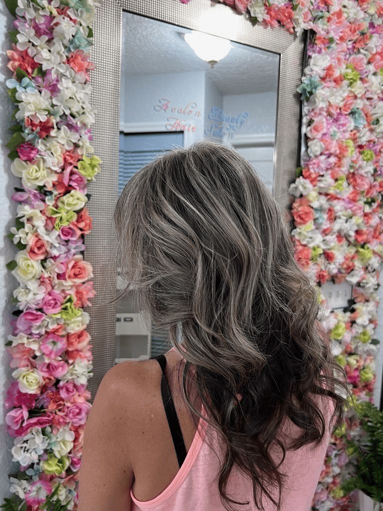 A woman is standing in front of a mirror with flowers on the wall behind her.