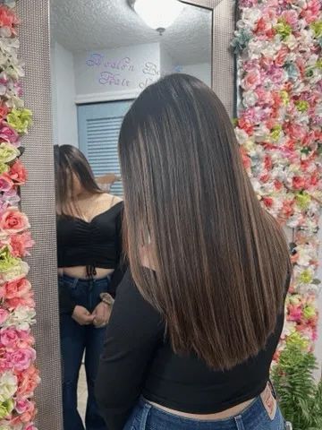 A woman is standing in front of a mirror in front of a wall of flowers.