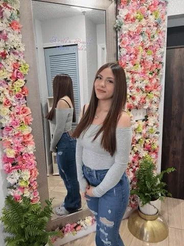 A woman is standing in front of a mirror in front of a wall of flowers.