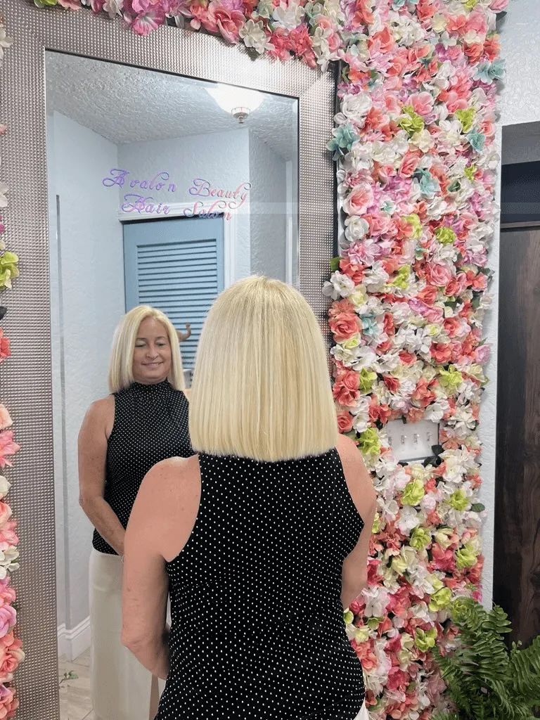 A woman is standing in front of a mirror with flowers on the wall behind her.