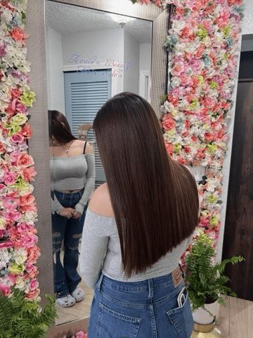 A woman is standing in front of a mirror in front of a wall of flowers.