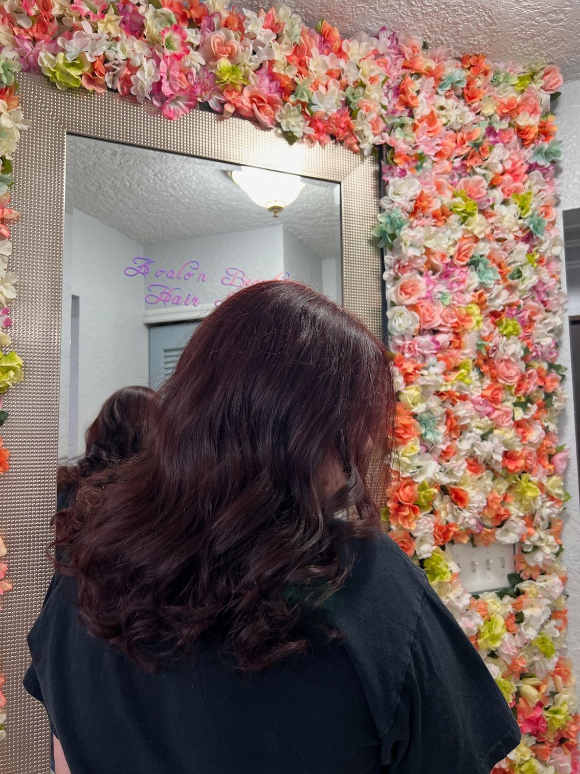 A woman is standing in front of a mirror in front of a wall of flowers.