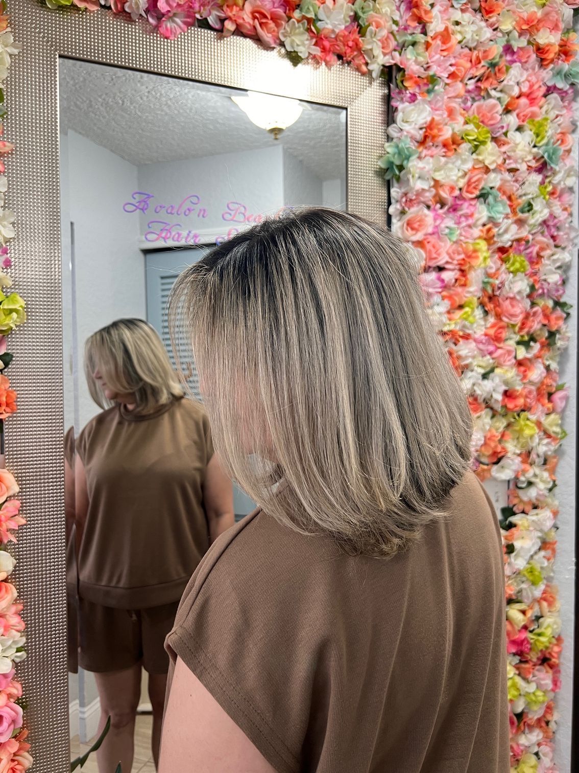 A woman is standing in front of a mirror with flowers on the wall behind her.