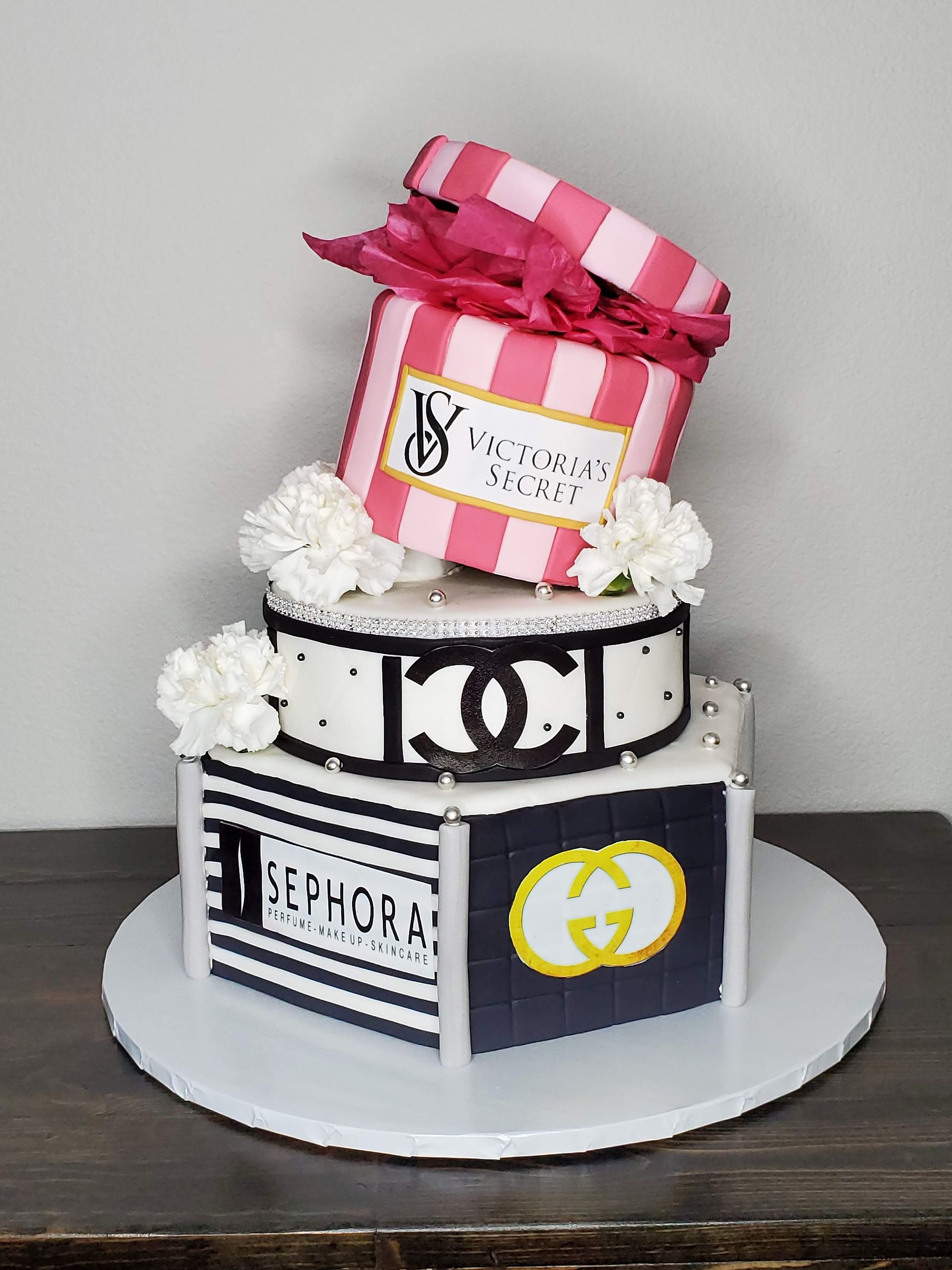 Three-tiered cake with Chanel, Sephora, Victoria's Secret, and Gucci branding. Pink and black colors.