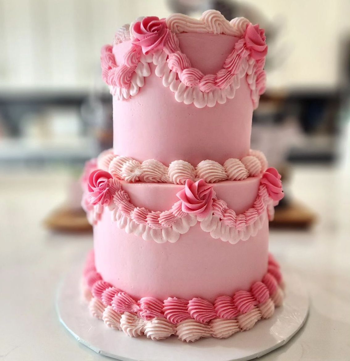 Two-tiered pink cake with frosting details and pink rosettes.