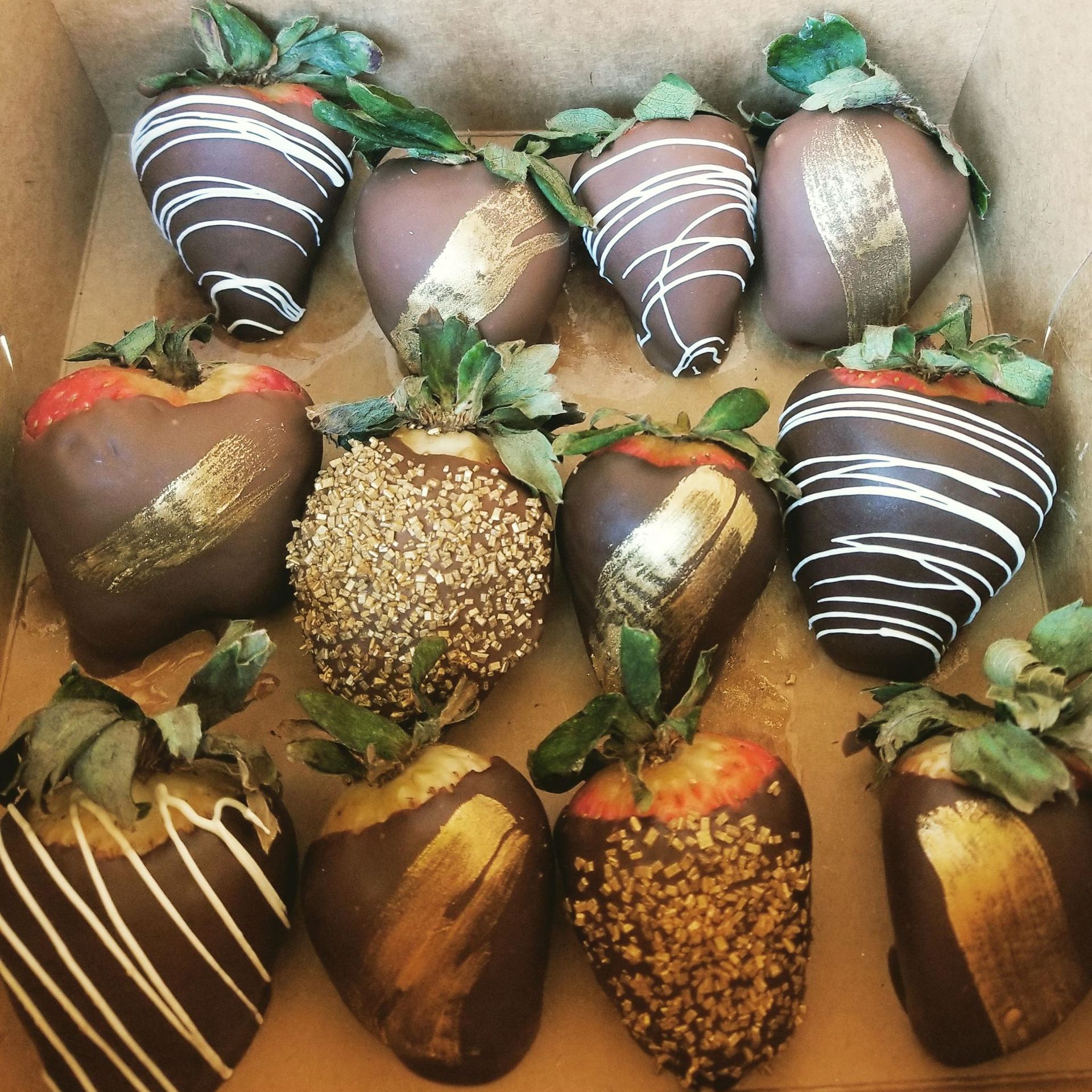 Chocolate-covered strawberries in a box, decorated with gold and white drizzle, and sprinkles.